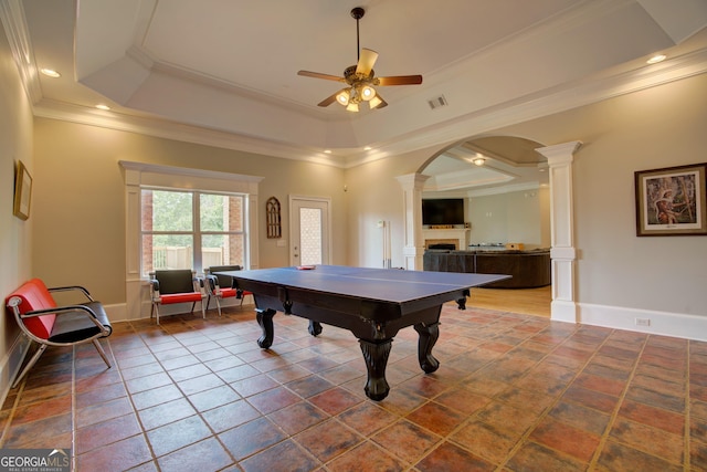 game room featuring ornate columns, a ceiling fan, ornamental molding, a fireplace, and a raised ceiling