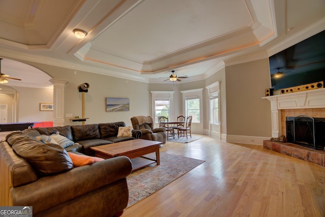 living room with a ceiling fan, arched walkways, light wood-style flooring, a fireplace, and a tray ceiling