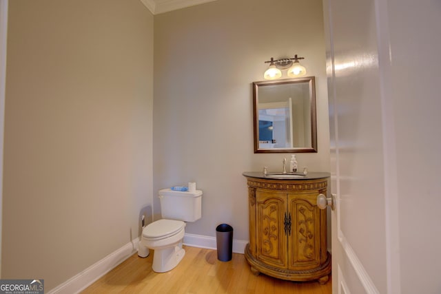 bathroom with toilet, wood finished floors, ornamental molding, vanity, and baseboards