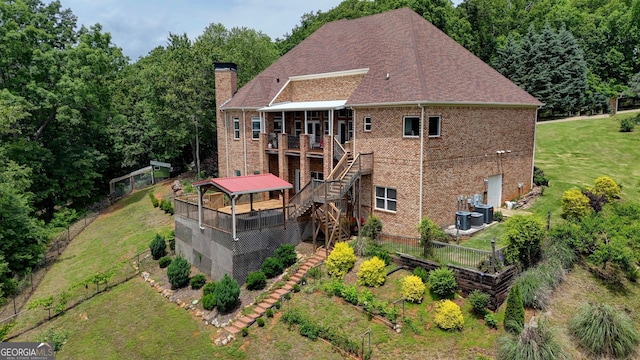 back of property with stairway, a wooden deck, a chimney, brick siding, and a lawn