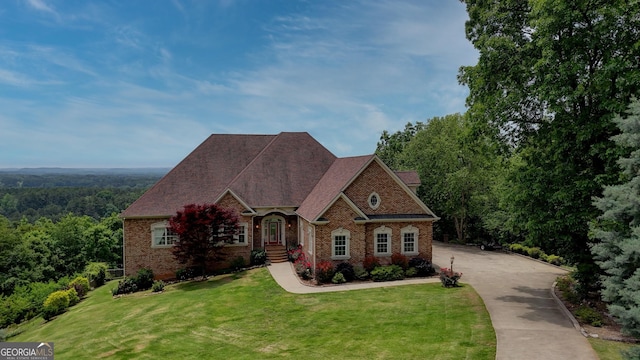 view of front of property with brick siding, a front lawn, concrete driveway, and a wooded view