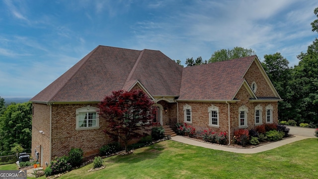 view of front of house with brick siding, a front yard, and roof with shingles