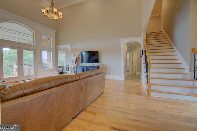 living room featuring arched walkways, a towering ceiling, french doors, stairway, and light wood-style floors