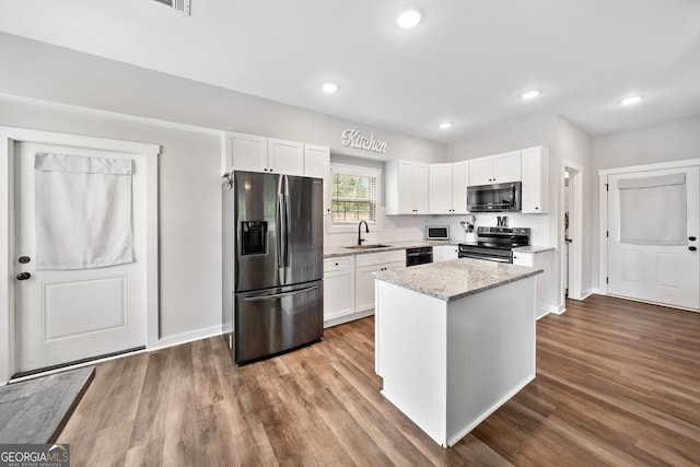 kitchen featuring stainless steel appliances, white cabinetry, light stone countertops, a center island, and dark wood-type flooring