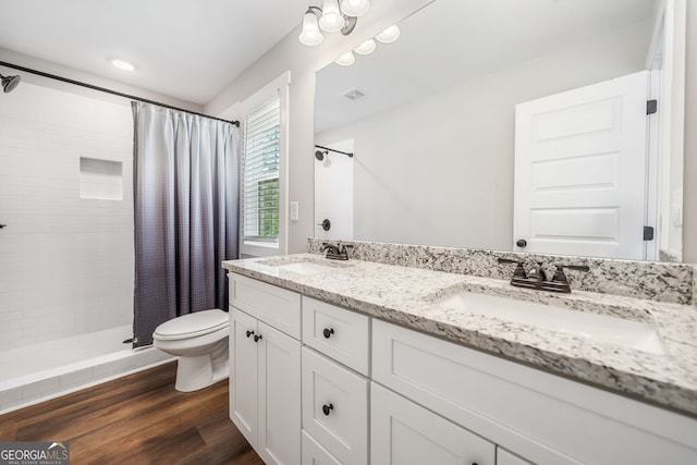 bathroom with toilet, tiled shower, double vanity, and wood finished floors
