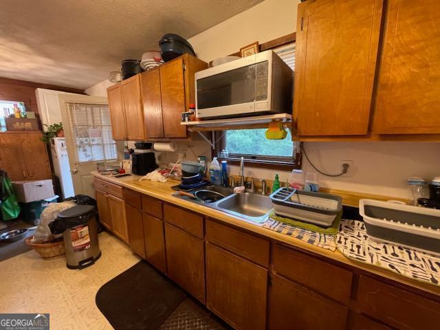 kitchen with stainless steel microwave, light countertops, a sink, and brown cabinets
