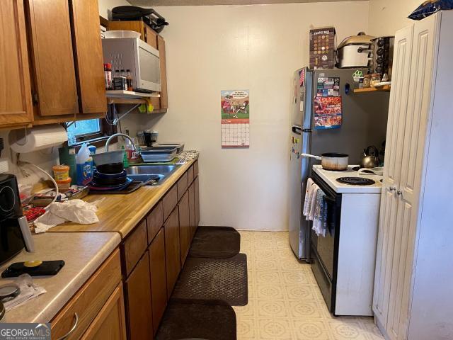 kitchen featuring electric stove, a sink, brown cabinets, light countertops, and light floors