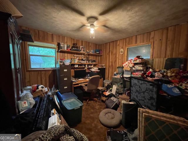 office with a ceiling fan, wooden walls, carpet, and a textured ceiling