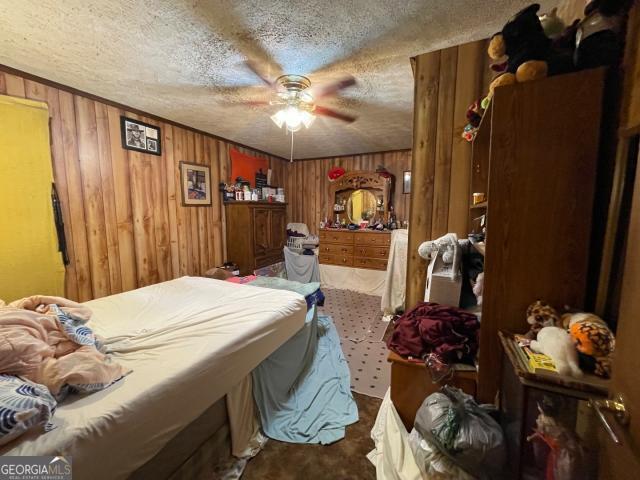 carpeted bedroom featuring wood walls, a textured ceiling, and a ceiling fan