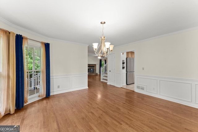 1713 Dudley Dr, Woodstock, GA 30188 - unfurnished room featuring a chandelier, crown molding, light wood finished floors, wainscoting, and a decorative wall