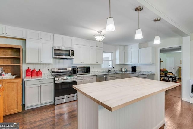 kitchen featuring stainless steel appliances, pendant lighting, dark wood-type flooring, a sink, and butcher block counters