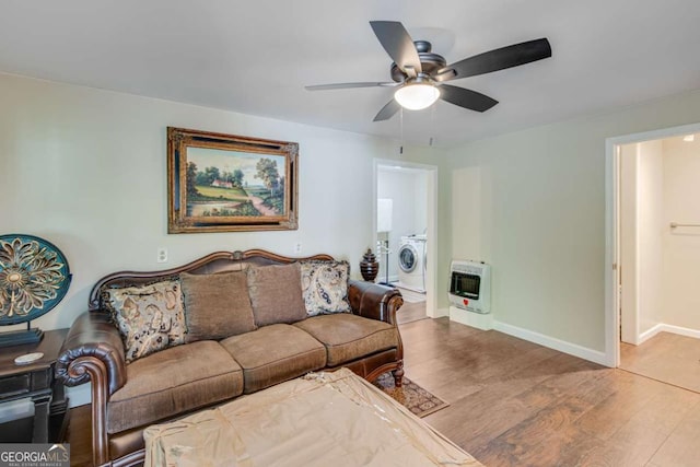 living room featuring washer / dryer, heating unit, wood finished floors, a ceiling fan, and baseboards