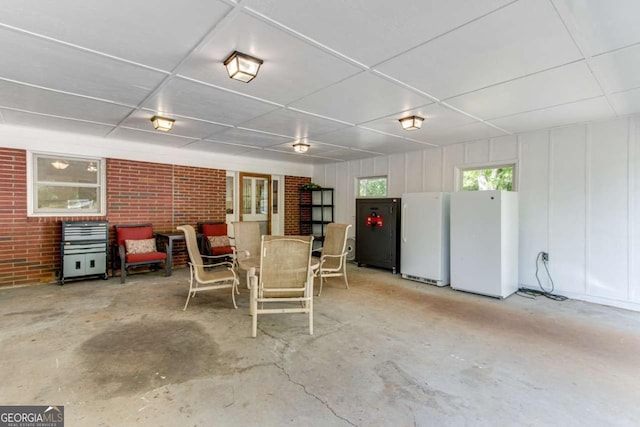 dining space featuring unfinished concrete floors, a paneled ceiling, and brick wall