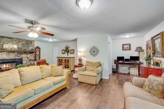 living area with a textured ceiling, wood finished floors, a ceiling fan, a stone fireplace, and an office area