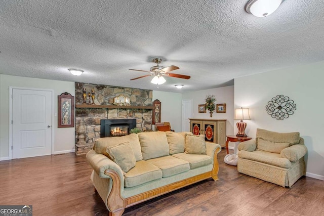 living area with a ceiling fan, wood finished floors, a fireplace, and a textured ceiling