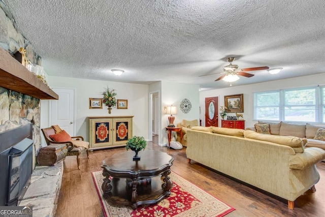 living room featuring a textured ceiling, a ceiling fan, wood finished floors, and a fireplace