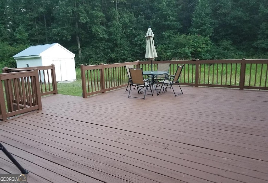1495 Martin Mill Rd, Newnan, GA 30263 - wooden deck with outdoor dining space, an outbuilding, a storage unit, a yard, and a wooded view