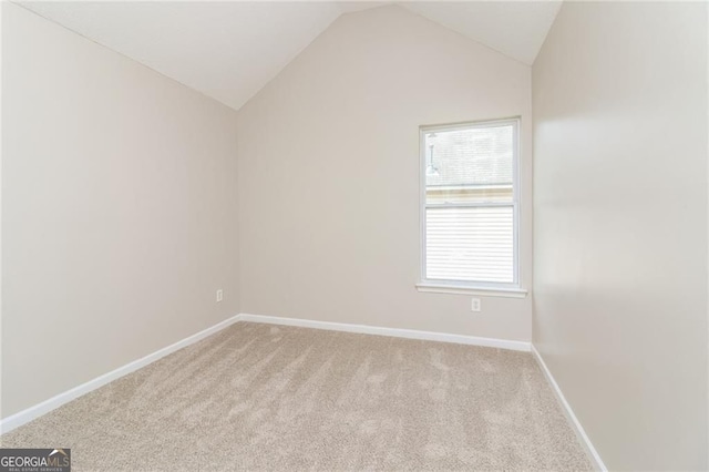 spare room featuring light colored carpet, vaulted ceiling, and baseboards