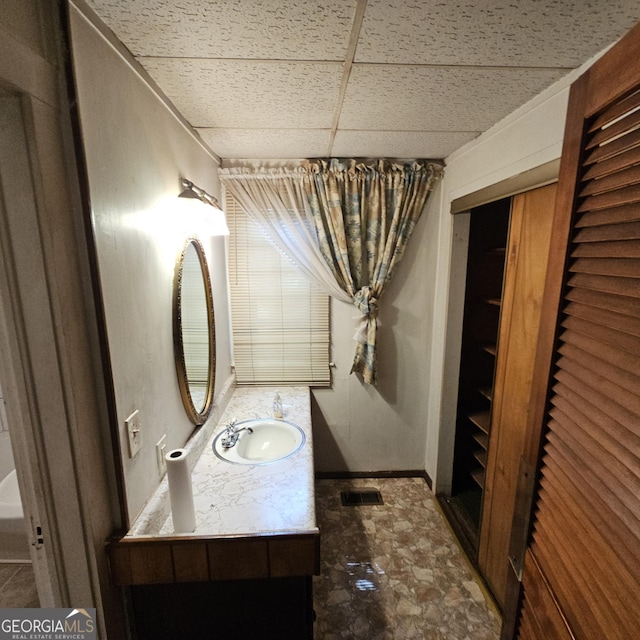 bathroom with a drop ceiling, stone finish flooring, and vanity