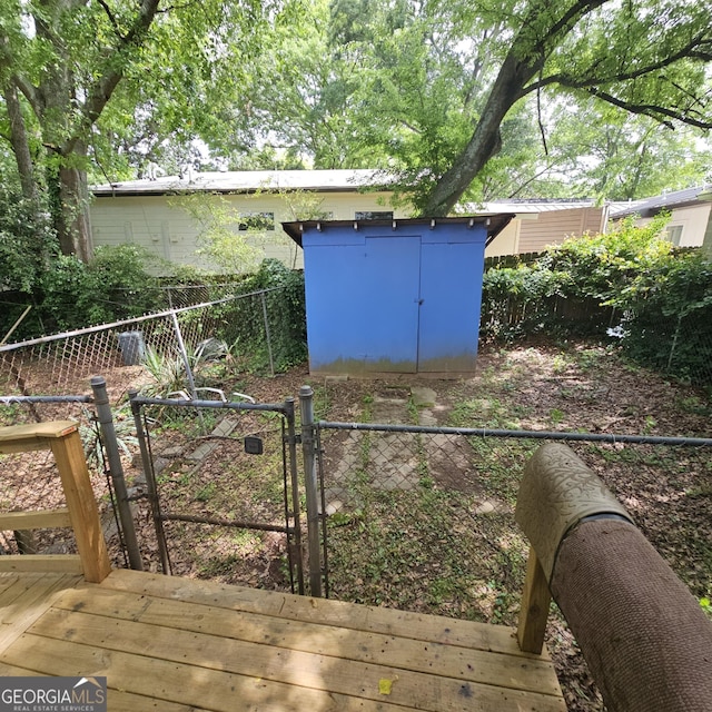 fenced backyard with a storage unit, a deck, an outbuilding, and a gate