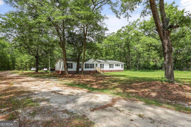 view of front of house featuring crawl space, driveway, a front yard, and a view of trees