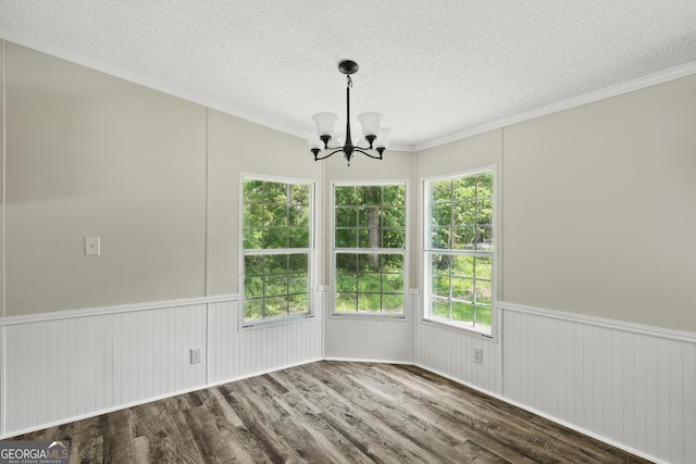 unfurnished dining area featuring a chandelier, a textured ceiling, wood finished floors, healthy amount of natural light, and crown molding