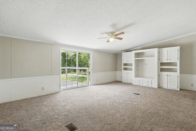 unfurnished living room featuring ceiling fan, ornamental molding, lofted ceiling, wainscoting, and light carpet
