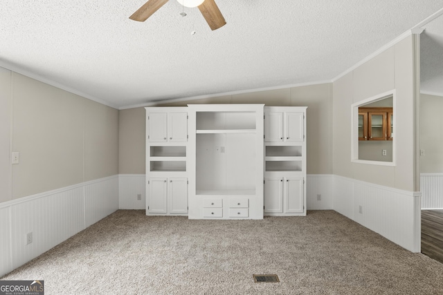 unfurnished bedroom with a wainscoted wall, crown molding, a textured ceiling, carpet flooring, and ceiling fan