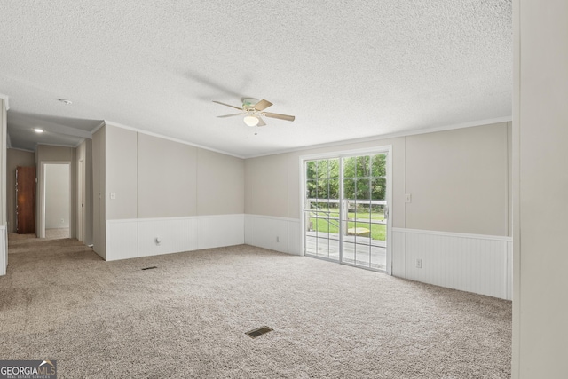 spare room featuring ceiling fan, crown molding, carpet floors, a wainscoted wall, and a textured ceiling