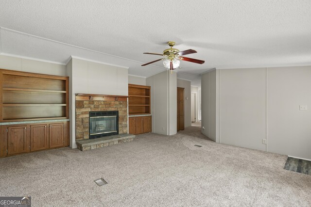 unfurnished living room featuring a ceiling fan, a textured ceiling, carpet, a fireplace, and ornamental molding
