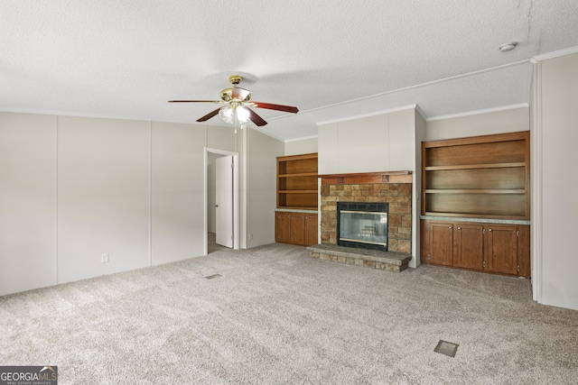 unfurnished living room featuring a textured ceiling, a ceiling fan, carpet, crown molding, and a glass covered fireplace