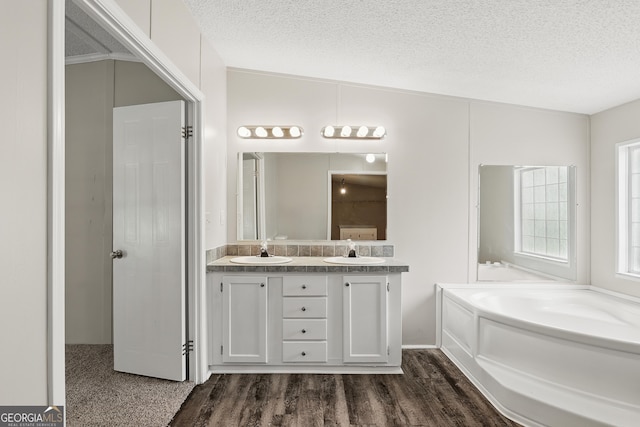 bathroom with wood finished floors, double vanity, a textured ceiling, and a garden tub