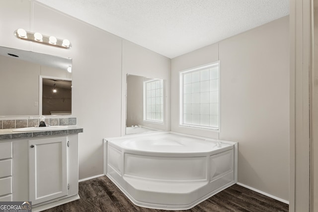 full bathroom featuring wood finished floors, a garden tub, vanity, a textured ceiling, and baseboards