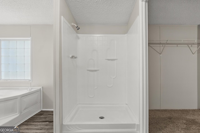 bathroom featuring a shower, a textured ceiling, a walk in closet, healthy amount of natural light, and wood finished floors