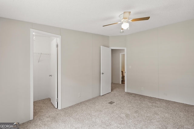 unfurnished bedroom featuring carpet, a spacious closet, a ceiling fan, and a closet