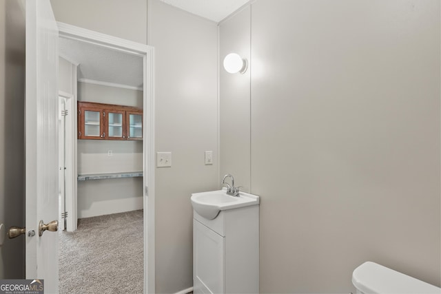 half bath featuring vanity, toilet, and ornamental molding