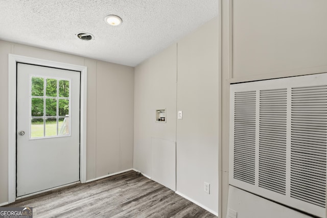 doorway to outside with a heating unit, a textured ceiling, and wood finished floors