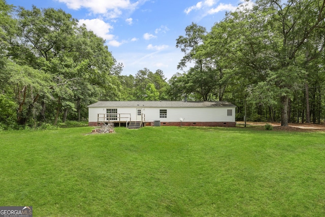back of house with crawl space, a deck, a yard, and a wooded view