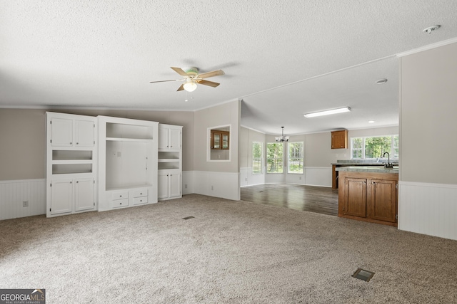 unfurnished living room with carpet flooring, wainscoting, a textured ceiling, ornamental molding, and ceiling fan