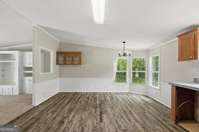 unfurnished dining area featuring a textured ceiling, a chandelier, ornamental molding, dark wood finished floors, and a wainscoted wall