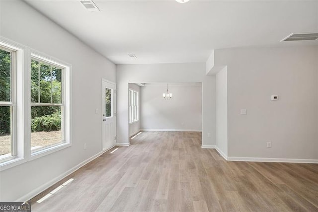 spare room with a chandelier, light wood-type flooring, and baseboards