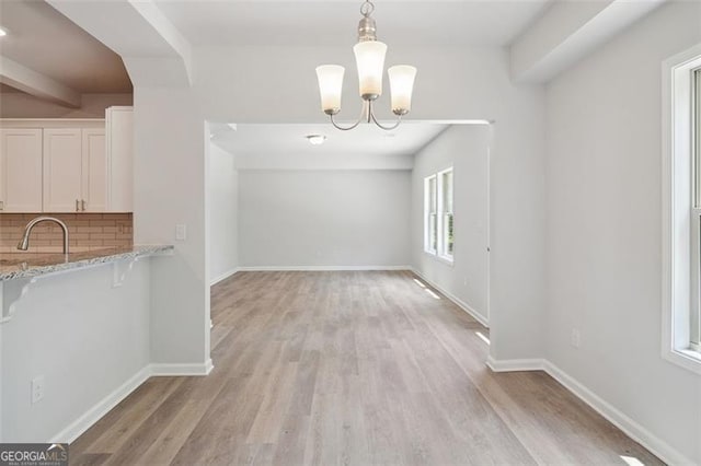 unfurnished dining area with light wood-style floors, a chandelier, a sink, and baseboards