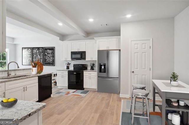kitchen with black appliances, a sink, white cabinetry, decorative backsplash, and light wood-style flooring