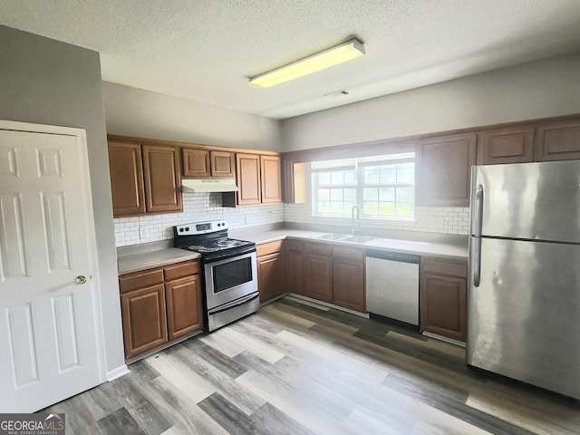 kitchen featuring stainless steel appliances, a sink, under cabinet range hood, light countertops, and backsplash