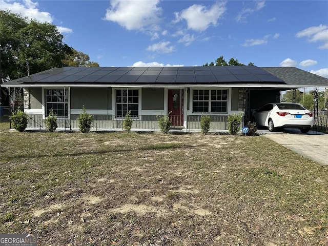 ranch-style home with covered porch, an attached carport, solar panels, concrete driveway, and a front yard