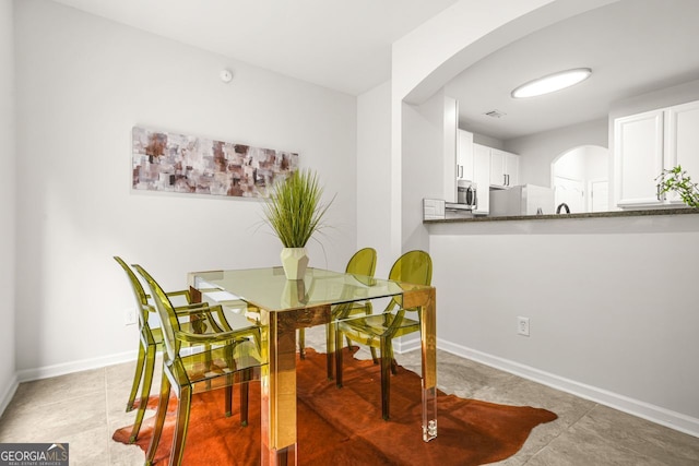 dining room with arched walkways, baseboards, and light tile patterned floors