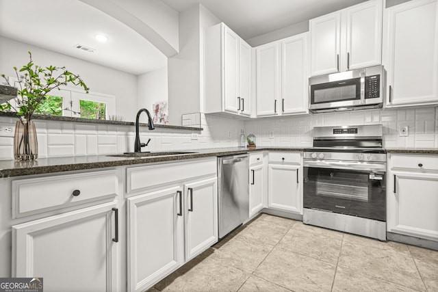 kitchen featuring appliances with stainless steel finishes, a sink, decorative backsplash, and white cabinetry
