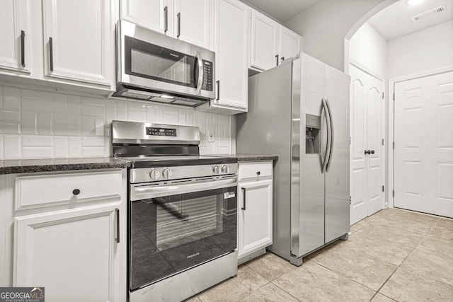 kitchen featuring stainless steel appliances, arched walkways, white cabinets, and dark stone counters