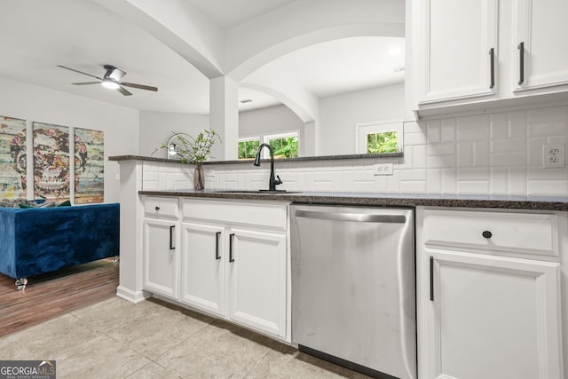 kitchen featuring stainless steel dishwasher, a sink, ceiling fan, dark stone countertops, and white cabinets