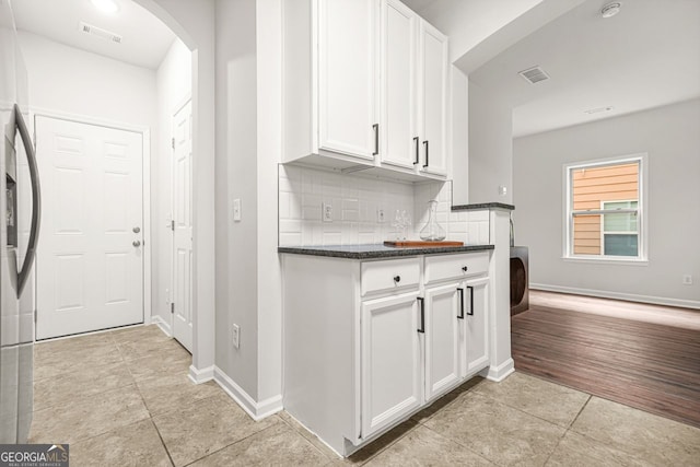 kitchen with light tile patterned floors, dark countertops, white cabinets, decorative backsplash, and arched walkways